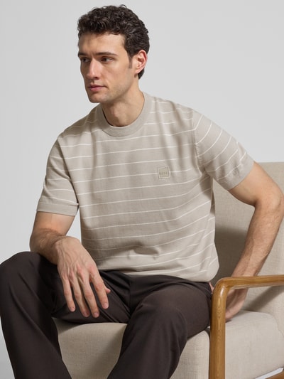 Mężczyzna prezentuje Regular Fit T-Shirt aus Baumwoll-Kaschmir-Mix Modell 'KANACHO' von BOSS Orange w jasnobeżowym kolorze z subtelnym, poziomym pasiastym wzorem i label patch na piersi, dzianina o gładkiej teksturze, okrągły dekolt, krótki rękaw, widok na górną część ciała z przodu.