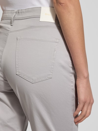 Männermodel trägt Flared Fit Spodnie materiałowe z mieszanki bawełny i lyocellu, model 'Carola' od BRAX, 5 kieszeni, zapięcie na guzik i zamek błyskawiczny, kolor jasnoszary, Szerokość w rozmiarze 36K: 37 cm, długość wewnętrzna nogawki 75 cm, detaliczne ujęcie tyłu.