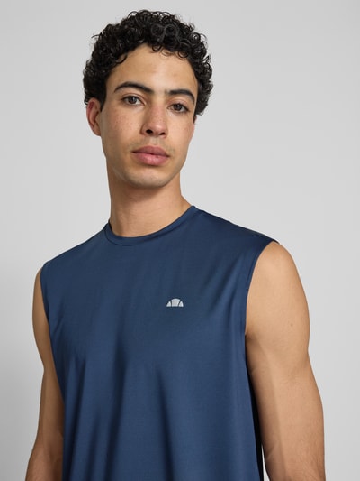 Męski model nosi Relaxed Fit Top mit Logo-Print model 'OLIOS' od Ellesse, elastyczna mieszanka materiałów w kolorze granatowym, okrągły dekolt, długość tyłu w rozmiarze M: 74 cm, z przodu nadruk z logo, zbliżenie na górną część ciała.
