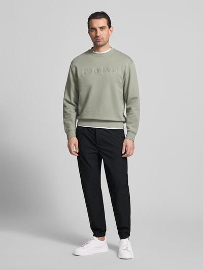 Männermodel trägt Slim Fit Schlupfhose mit Gesäßtasche von CK Calvin Klein in Schwarz, elastischer Bund, Ganzkörperansicht von vorne.