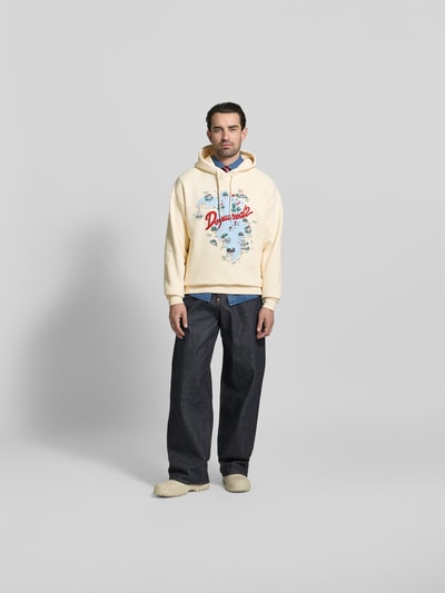 Männermodel trägt Relaxed Fit Hoodie mit Logo-Print von Dsquared2 in Creme, Reine Baumwolle, Kapuze mit Tunnelzug, elastische Abschlüsse, Rückenlänge 71 cm, Ganzkörperansicht von vorne.