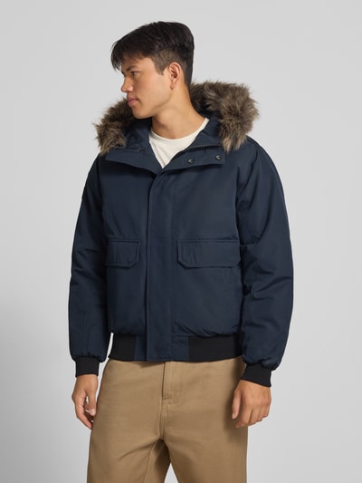 Männermodel trägt dunkelblaue Bomberjacke mit Label-Patch Modell 'Everest' von Superdry, Kunstfellkapuze, Pattentaschen, Ganzkörperansicht von vorne. Herren Bomberjacke, Regular Fit, Reiß- und Druckknopfverschluss.