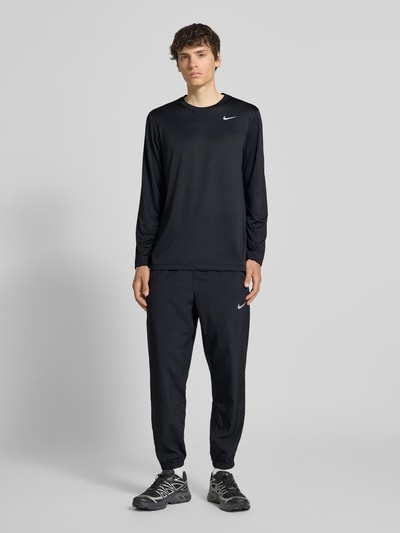 Męski model nosi Form Pants mit Logo-Print und Eingrifftaschen von NIKE TRAINING, czarny kolor, dopasowany krój, elastyczny pas, wpuszczane kieszenie, elastyczne wykończenia, długość wewnętrzna nogawki w rozmiarze M: 38 cm, Ganzkörperansicht von vorne.