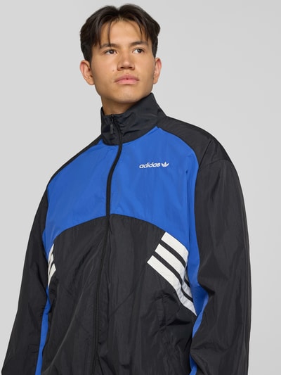 Männermodel trägt Regular Fit Trainingsjacke im Two-Tone-Design Modell 'MUC TT' von adidas Originals in Blau und Schwarz, Nahaufnahme Oberkörper, Herren Trainingsjacke von adidas Originals