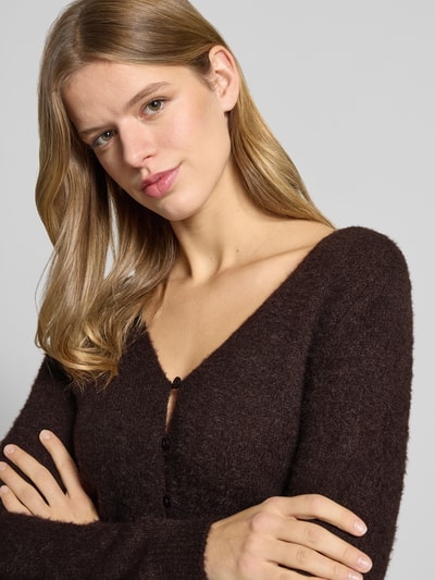 Frauenmodel trägt Slim Fit Strickjacke mit einreihige Knopfleiste Modell 'KERRY' von Only, Optik: unifarben, V-Ausschnitt, Langarm, Materialverarbeitung: Strick, Label Patch, Nahaufnahme Oberkörper.