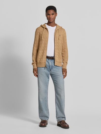 Męski model nosi Regular Fit Strickjacke aus reiner Baumwolle von Polo Ralph Lauren w kolorze beżowym, tekstura dzianiny, Ganzkörperansicht von vorne.