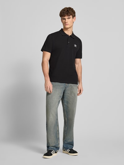 Männermodel trägt Regular Fit Poloshirt mit Logo-Stitching von adidas Originals in Schwarz, reine Baumwolle, Ganzkörperansicht von vorne.