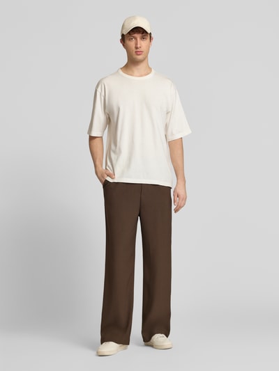 Männermodel trägt braune Stoffhose mit Logo-Bund und Gesäßtaschen von ANOTHER COTTON LAB aus Material-Mix mit Stretch-Anteil, Wide-Fit, Ganzkörperansicht von vorne.