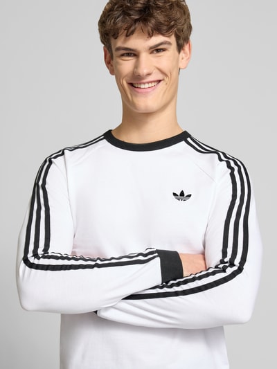 Männermodel trägt Longsleeve mit Label-Stitching von adidas Originals in Weiß mit schwarzen Details, reine Baumwolle, Nahaufnahme Oberkörper.