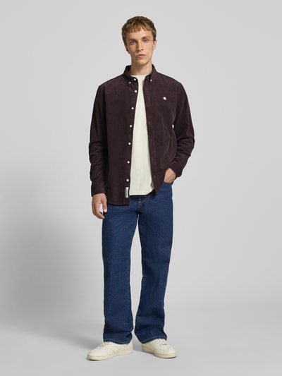 Mężczyzna nosi Regular Fit Freizeithemd aus Cord mit Button-Down-Kragen von Carhartt Work In Progress, bawełna, krój regular fit, model 'Madison', cord, logo haft, długość tyłu w rozmiarze M: 76 cm, szerokość w rozmiarze M: 44 cm, długość rękawa w rozmiarze M: 64 cm, widok całej sylwetki z przodu.