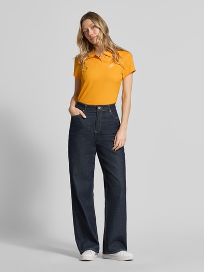 Vrouwenmodel draagt 'Slim Fit poloshirt uit katoenmix' van Tommy Hilfiger in effen kleuren, gestikt logo, korte mouw, piqué, voorkant, volledige lichaamsopname.