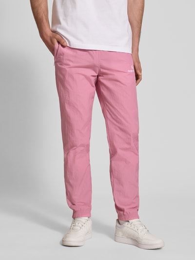 Männermodel trägt Straight Fit Stoffhose mit Logo-Stitching Modell 'Nayla' von SERGIO TACCHINI, rosa, Strukturstoff, Ganzkörperansicht von vorne, Herren Stoffhose, elastischer Bund mit Tunnelzug, elastische Beinabschlüsse, Innenbeinlänge bei Größe M 77 cm.