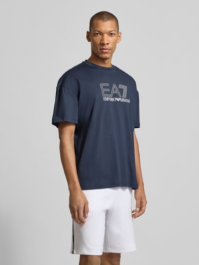 Männermodel trägt T-Shirt mit Logo und Rundhalsausschnitt von EA7 Emporio Armani in Dunkelblau, Regular-Fit, Reine Baumwolle, Ganzkörperansicht von vorne.