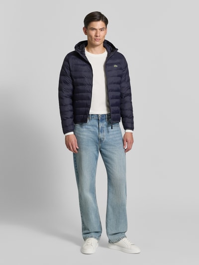 Männermodel trägt Regular Fit Bomberjacke mit down-Füllung von Lacoste, unifarben, Kapuzenkragen, wasserabweisend, Ganzkörperansicht von vorne.