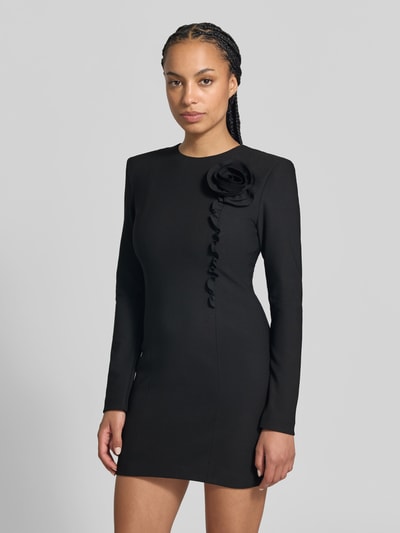 Frauenmodel trägt Slim Fit Minikleid mit floralem Besatz von ROTATE, schwarzer elastischer Stoff, Langarm, Rundhalsausschnitt, Ganzkörperansicht von vorne.