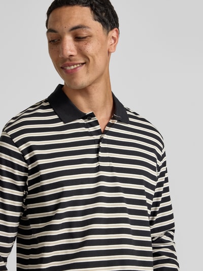 Mannelijk model draagt Regular Fit poloshirt met streepmotief model 'CASSIS' van Jack & Jones, puur katoen, shirt met lange mouwen, knoopsluiting, ruglengte bij maat M 66 cm, kleuren zwart en beige, detailopname bovenlichaam.