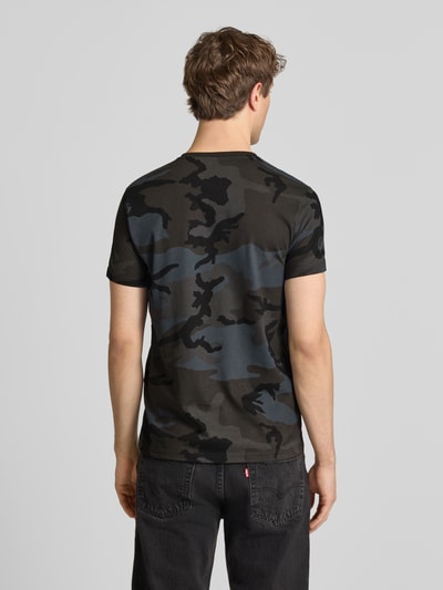 Männermodel trägt T-Shirt mit Label-Print von Alpha Industries in Grau-Schwarz Camouflage, Reine Baumwolle, Gerader-Schnitt, Rückenlänge 70 cm, Ganzkörperansicht Rückansicht.