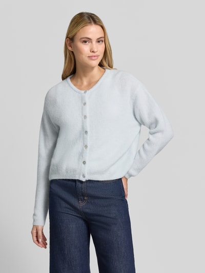 Frauenmodel trägt Relaxed Fit Strickjacke aus Woll-Mix mit Leinen-Anteil von American Vintage in Hellblau, gerippte Bündchen, Ganzkörperansicht von vorne.