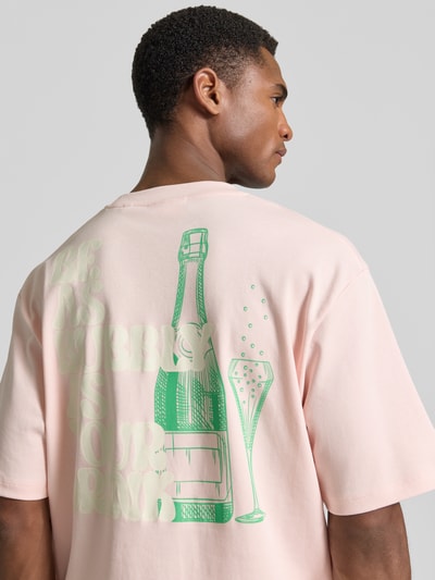 Männermodel trägt Oversized T-Shirt mit Label-Print von Lindbergh in zartem Rosa, Reine Baumwolle, Rundhalsausschnitt, Rückenlänge 70 cm, Ganzkörperansicht Rückansicht.