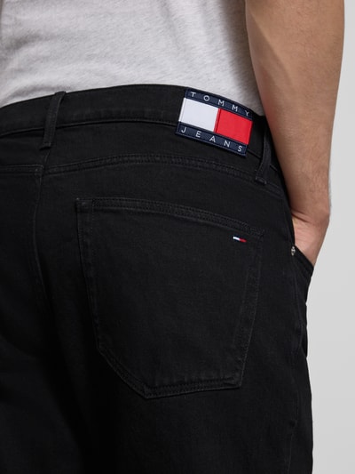 Männermodel trägt Straight Fit Jeans aus Baumwoll-Mix Modell 'RYAN' von Tommy Jeans in Schwarz mit Label Patch und 5-Pocket-Design, Nahaufnahme Rückansicht.
