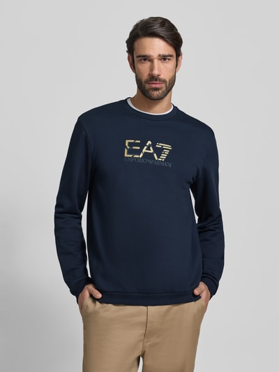 Männermodel trägt Sweatshirt mit Logo und Rundhalsausschnitt von EA7 Emporio Armani in Dunkelblau, reine Baumwolle, Regular Fit, Nahaufnahme Oberkörper.
