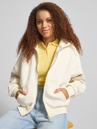 Frauenmodel trägt Relaxed Fit Sweatjacke mit geteilter Kängurutasche von Review im Baumwoll-Mix, elastische Abschlüsse, Kapuze, überschnittene Schultern, cremiges Beige, glatte Struktur, Ganzkörperansicht von vorne.
