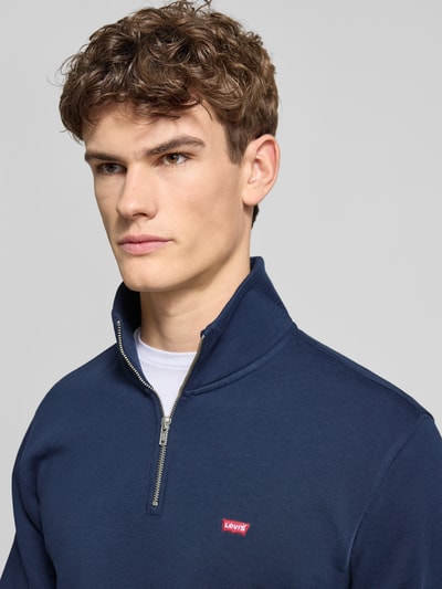 Männermodel trägt Regular Fit Troyer aus reiner Baumwolle von Levi's® in Dunkelblau mit Stehkragen, Reißverschluss, Label-Detail, Nahaufnahme Oberkörper.