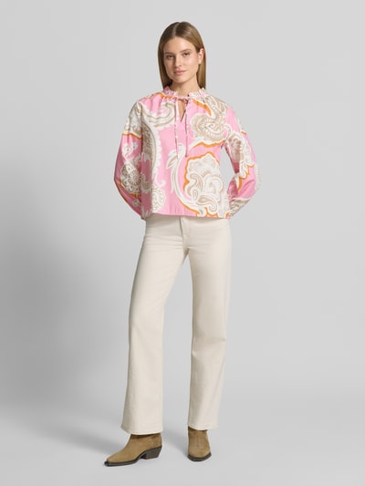 Modelka kobieca ma na sobie Regular Fit Bluse mit Allover-Paisley-Print od Emily Van den Bergh, różowe i kremowe wzory, bawełna, długi rękaw, stójka z falbanką, zapięcie na pętelkę, kremowe spodnie, beżowe botki, całopostaciowy widok z przodu.