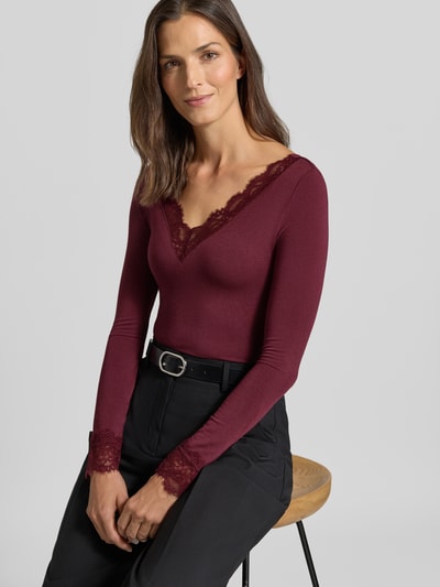 Kobiece model prezentuje bluzkę z długim rękawem z mieszanki modalu z dodatkiem wełny model 'SKYE' od VERO MODA w kolorze bordo, tekstura gładka, czarne spodnie, damska bluzka z długim rękawem, widok na górną część ciała z przodu