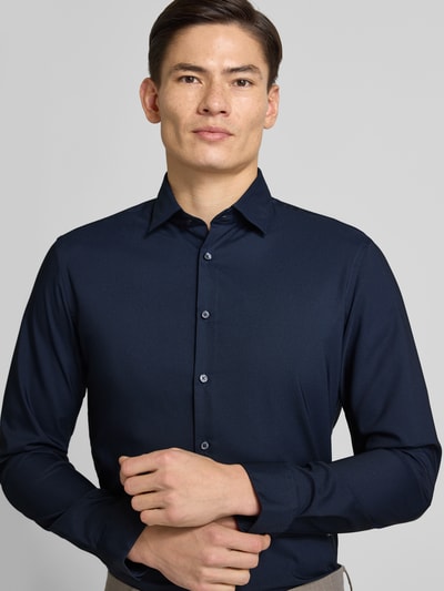 Männermodel trägt Slim Fit Business-Hemd mit Kentkragen von Jake*s, dunkelblauer Material-Mix mit Stretch-Anteil, Langärmlig, Durchgehende Knopfleiste, Sportmanschetten, Ganzkörperansicht von vorne.