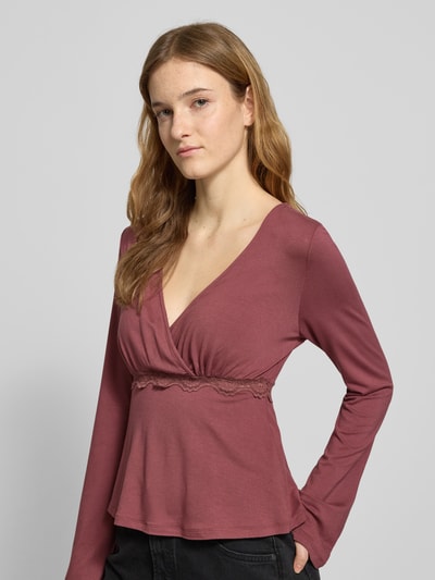 Vrouwenmodel draagt Slim Fit Langarmshirt uit viscosemix model 'SINI' van Only in wikkel-look met kanten details, diepe V-hals, label stitching, langem mouw, viscosemix, kleur oudroze, vooraanzicht borst close-up.