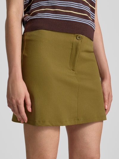 Frauenmodel trägt Slim Fit Minirock mit Reißverschluss von Gina Tricot in Olivgrün, elastischer Material-Mix, Nahaufnahme Oberkörper.