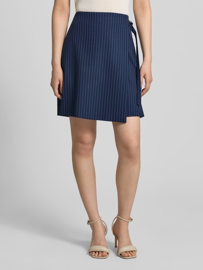 Frauenmodel trägt Leicht ausgestellter Mini-Rock in Wickeloptik Modell 'RABISU' von HUGO, dunkelblau mit Nadelstreifen-Muster, Bindegürtel, Twill, Optik:Allover-Muster, Passform: Regular-Fit, Mini-Länge, Reißverschluss, asymmetrischer Saum, Materialverarbeitung: Twill, Ganzkörperansicht von vorne.