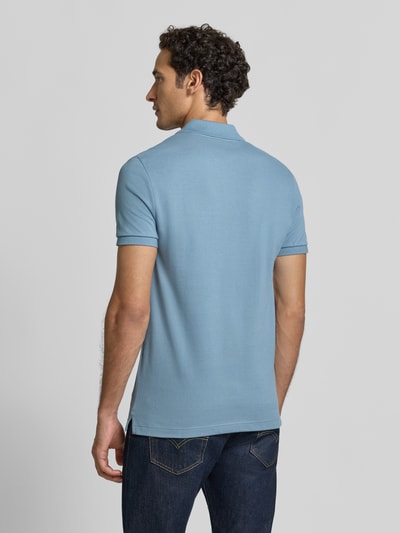 Männermodel trägt Slim Fit poloshirt uit puur katoen van Lacoste in lichtblauw, donkere jeans, Ganzkörperansicht Rückansicht.