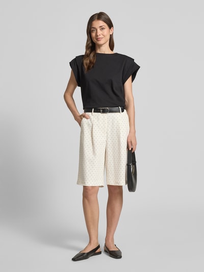 Frauenmodel trägt Bermudas im Allover-Look Modell 'Anja' von FREE/QUENT in Weiß mit schwarzen Punkten, weitem Bein, elastischem Bund, Paspeltaschen am Gesäß, Bundweite 38 cm, Innenbeinlänge 30 cm, kombiniert mit schwarzem Oberteil, Ganzkörperansicht von vorne.