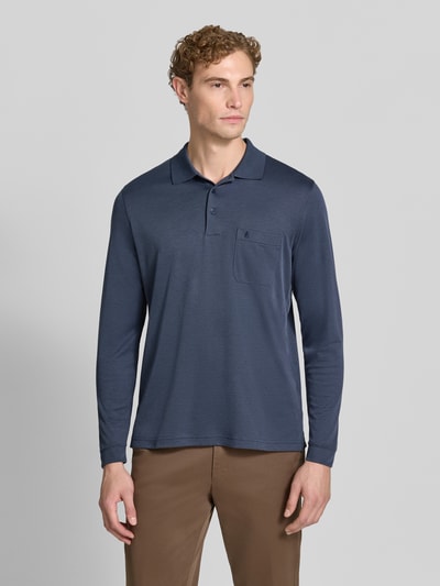 Männermodel trägt Regular Fit Poloshirt aus Baumwoll-Mix von RAGMAN in Dunkelblau, Brusttasche, elastische Abschlüsse, Ganzkörperansicht von vorne. Rückenlänge bei Größe M: 70 cm, langärmeliges Design.