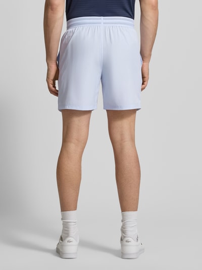 Męski model nosi Loose Fit Sport-Shorts mit Mesh-Bund od Lacoste, jednokolorowy, wyhaftowane logo, elastyczny pas z siateczki, wpuszczane kieszenie, widok całej sylwetki z tyłu.