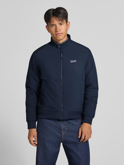 Männermodel trägt dunkelblauen bomberjack met Opstaande kraag, ritssluiting en logo, Model 'BROOKLYN' van JACK & JONES, regular fit, Ruglengte bij maat M: 67 cm, schouderbreedte: 49 cm, borstwijdte: 59 cm, mouwlengte: 66 cm, Ganzkörperansicht van voren.