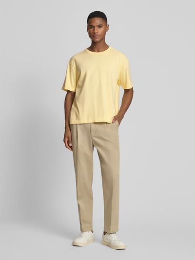 Männermodel trägt Cropped T-Shirt mit Rundhalsausschnitt von GAP in Gelb, aus reiner Baumwolle, kombiniert mit beigefarbener Hose, Ganzkörperansicht von vorne.