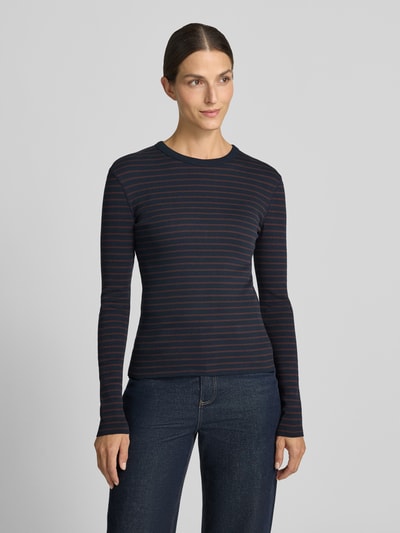 Frauenmodel trägt Slim Fit Longsleeve aus reiner Baumwolle Modell 'NURIT' von DRYKORN, feine Streifen in Dunkelblau und Rot, Rundhalsausschnitt, weiche Textur, Oberteil auf Jeans kombiniert, Damen Longsleeve, Ganzkörperansicht von vorne.