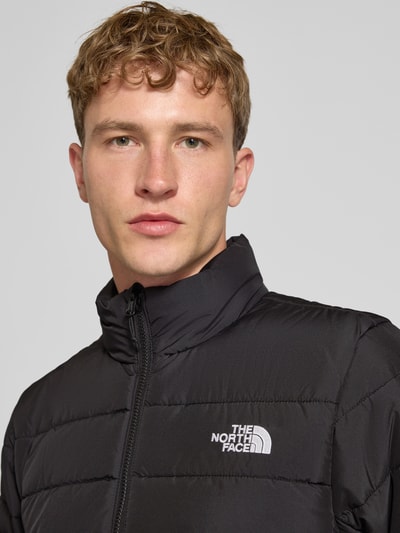 Männermodel trägt Regular Fit Jacke in Stepp-Optik Modell 'ACONCAGUA' von The North Face, schwarze Farbe mit Logo-Stitching, Nahaufnahme Oberkörper.