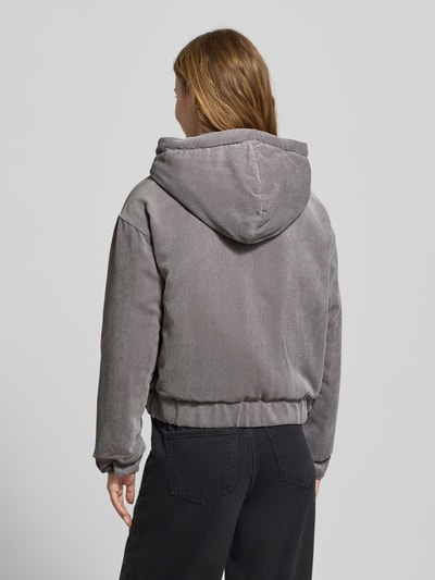 Frauenmodel trägt Regular Fit Bomberjacke mit Kapuze Modell 'SUVA' von Only aus grauem Cord mit Label Stitching, Ganzkörperansicht Rückansicht.