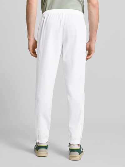 Männermodel trägt weißen Regular Fit Trainingsanzug mit Logo-Detail von Lacoste Sport, elastische Bündchen, Ganzkörperansicht Rückansicht.