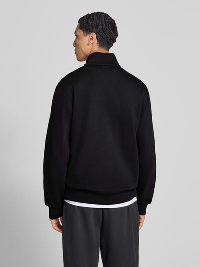 Männermodel trägt schwarzes Sweatshirt mit Label-Details von Champion, Troyer-Kragen, seitliche Eingrifftaschen, Rückenansicht, Baumwollmischung.