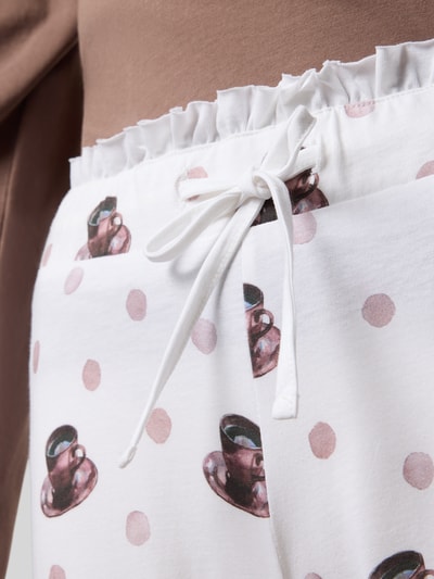 Frauenmodel trägt Regular Fit Pyjama aus reiner Baumwolle Modell 'Meine Auszeit' von LOUIS & LOUISA mit Statement-Stitching, Zierschleife, Rundhalsausschnitt, weißen Stoff mit rosa Punkten und braunen Tassenmotiven, Nahaufnahme Oberkörper.