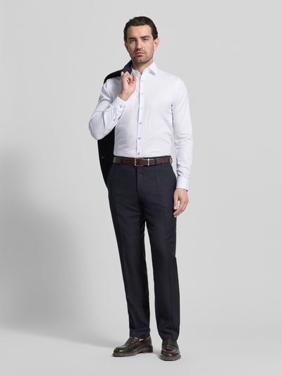 Męski model nosi Slim Fit Businesshemd mit Kentkragen od OLYMP No. Six, biały, długi rękaw, elastyczna bawełna, pełna listwa guzikowa, sportowe mankiety, długość pleców 81 cm, szerokość ramion 43 cm, długość rękawa 67 cm, krój slim fit, widok całej sylwetki z przodu.