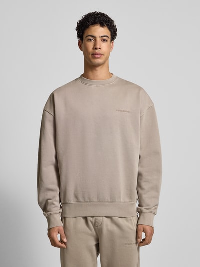 Männermodel trägt Oversized Sweatshirt mit Label-Stitching von Pegador in Beige, Baumwoll-Mix, Rundhalsausschnitt, gerippte Abschlüsse, Ganzkörperansicht von vorne.