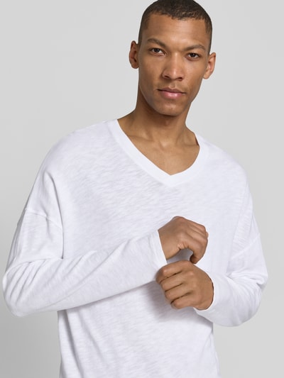 Männermodel trägt weißes Longsleeve mit V-Ausschnitt und überschnittenen Schultern, Modell 'SONOMA' von American Vintage aus Reine Baumwolle, Regular-Fit, Rückenlänge bei Größe M/L 66 cm, Nahaufnahme Oberkörper.