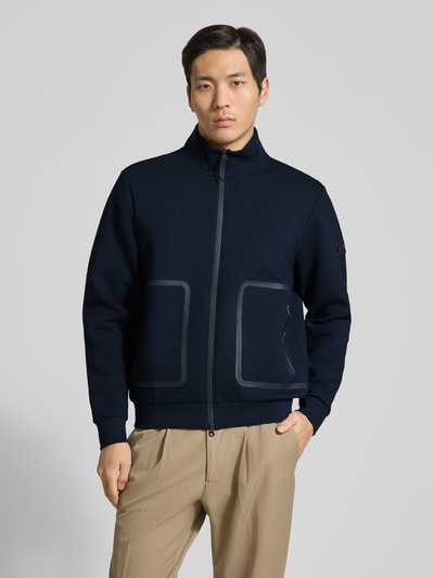Męski model nosi Regular Fit Jacke mit Stehkragen Modell 'Scott' od Peuterey, granatowy kolor, elastyczny materiał z bawełną, kieszenie, dwukierunkowy zamek, elastyczne wykończenia, długość tyłu 66 cm, długość rękawa 66 cm, widok całej sylwetki z przodu.