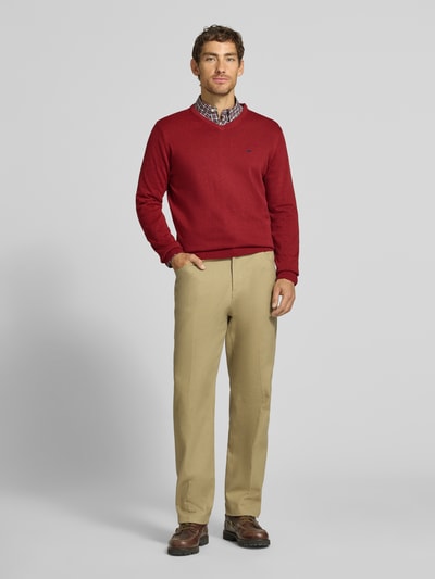 Männermodel trägt Strickpullover mit Label-Strickerei von Fynch-Hatton in Rot, reine Baumwolle, V-Ausschnitt, Ganzkörperansicht von vorne.